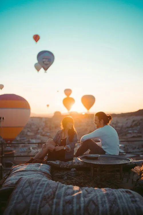 Couple sitting with hot air balloons at sunset